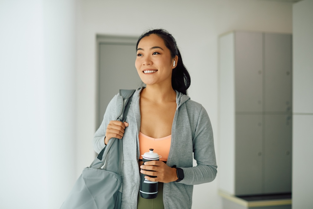 Happy sportswoman standing in locker room at the gym and looking away.