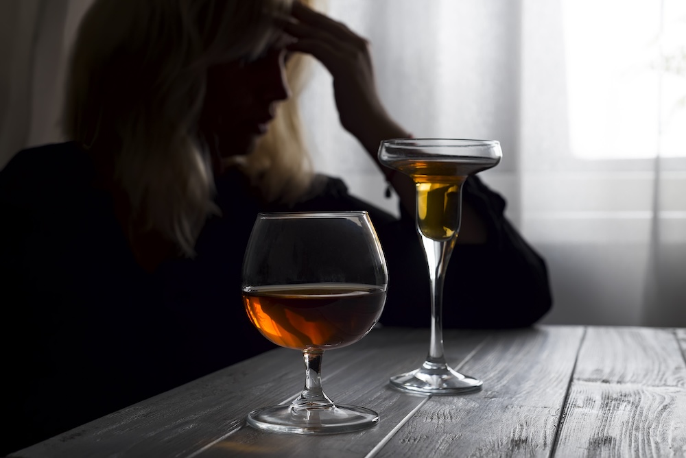 Woman struggling with alcohol addiction, drinking alone and looking out her window