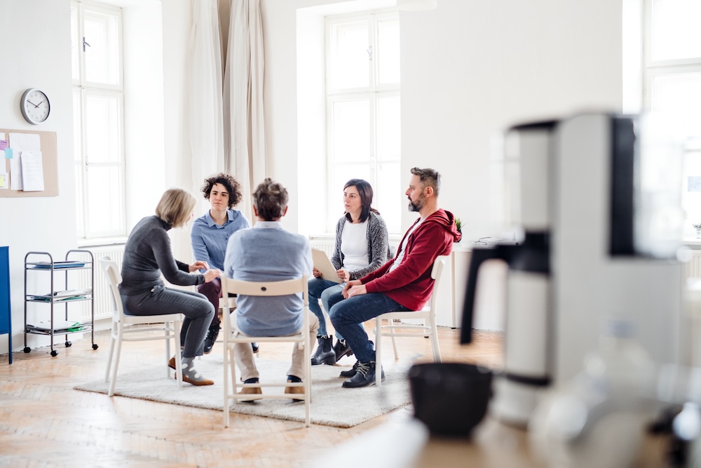 Adult men and women sitting in a circle during group therapy, talking.