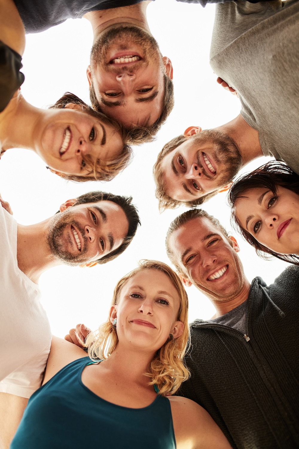 Group of individuals standing in a circle, smiling and looking down at the camera