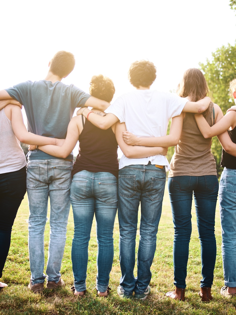 Group of friends holding each other, standing in the grass outside