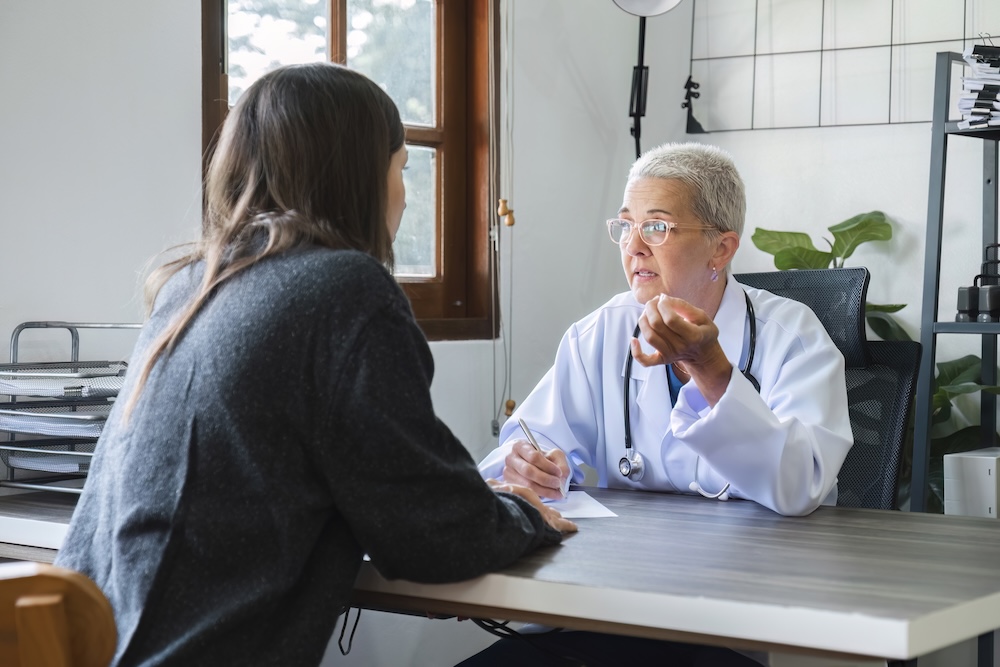 Female doctor in white coat talking with patient in clinic, giving advice