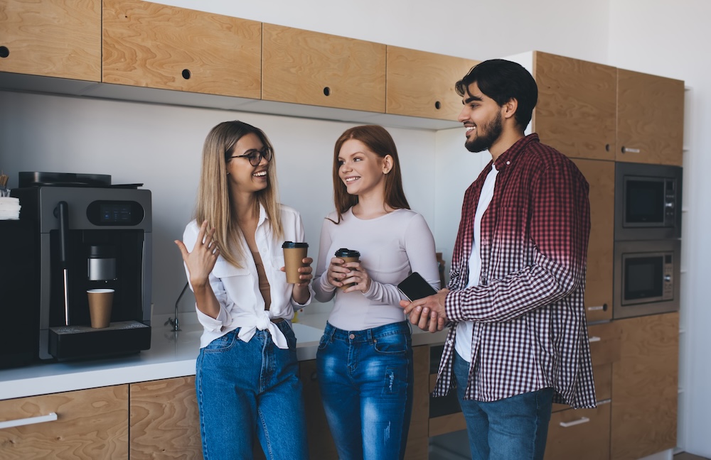 Happy young adults drinking coffee and looking at each other while talking in kitchen