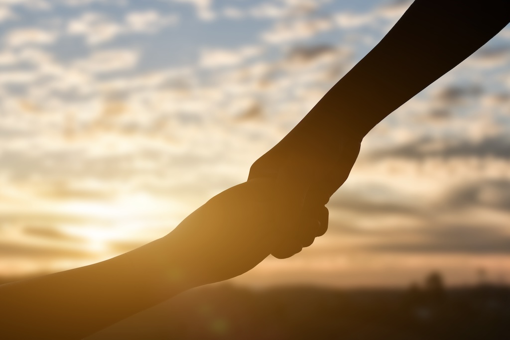 Silhouette of giving a help hand, hope and support each other over sunset background.