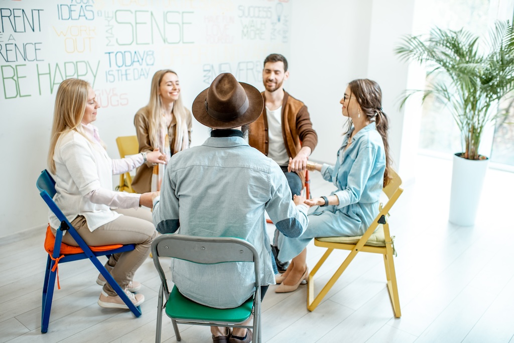 Group of diverse people keeping hands together, sitting in a circle during the psychological 12step therapy support group session, feeling support from each other