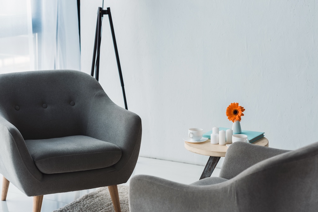 Cozy therapy office in light tones with grey chairs and table at mental health treatment center.