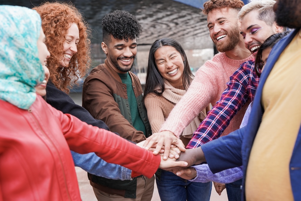 Group of young people stacking hands outdoors, signaling strength in community through their experiences in sober living.