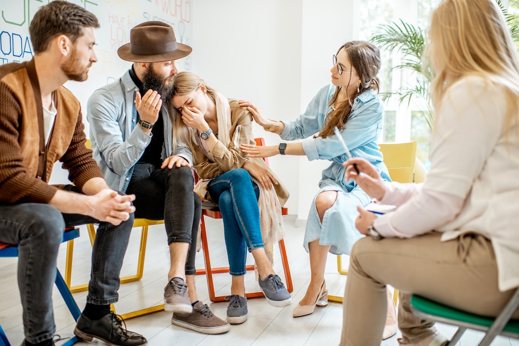 Young woman crying during the psychological therapy with group of people supporting her in support group during detox.