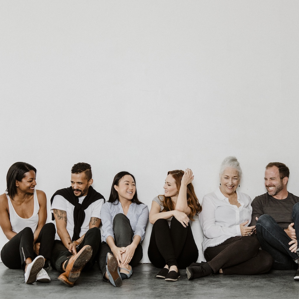 Group of cheerful diverse people sitting on a floor in a white room as part of mental health support group.