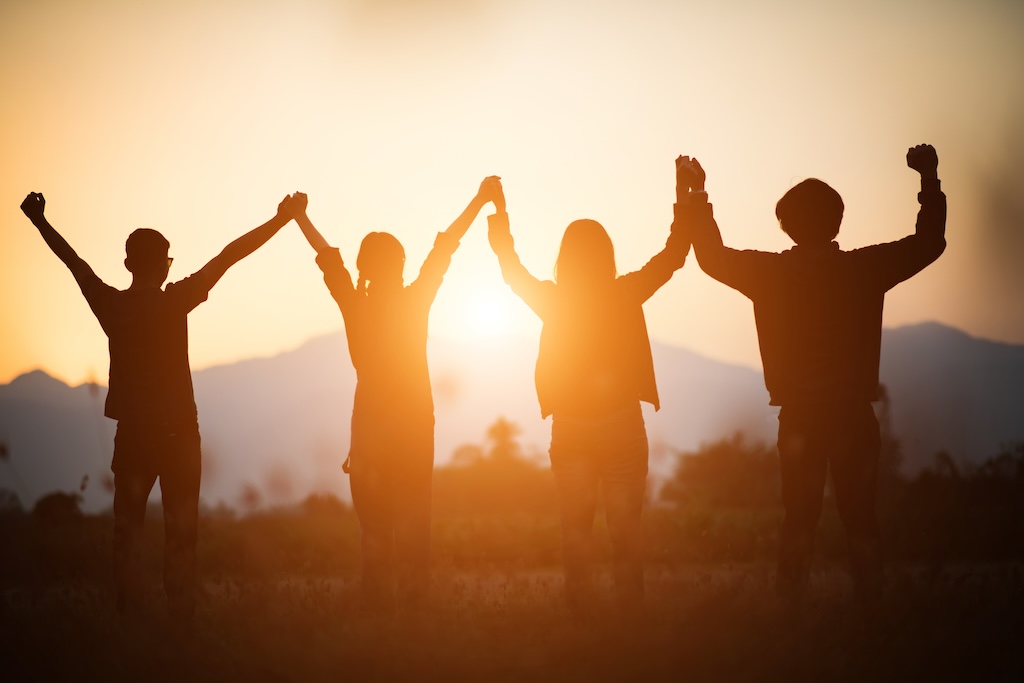 Silhouette of happy group of clients with their hands in the air at sunset symbolizing freedom in recovery from mental health conditions