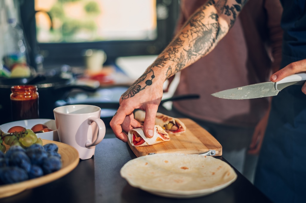 Cropped shot of a tattooed man hands cooking and making breakfast in the kitchen.