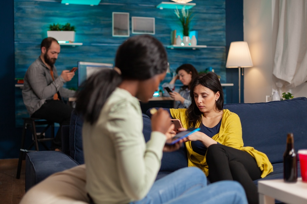 Group of people with social anxiety disorder browsing on mobile phones while sitting in a room together.