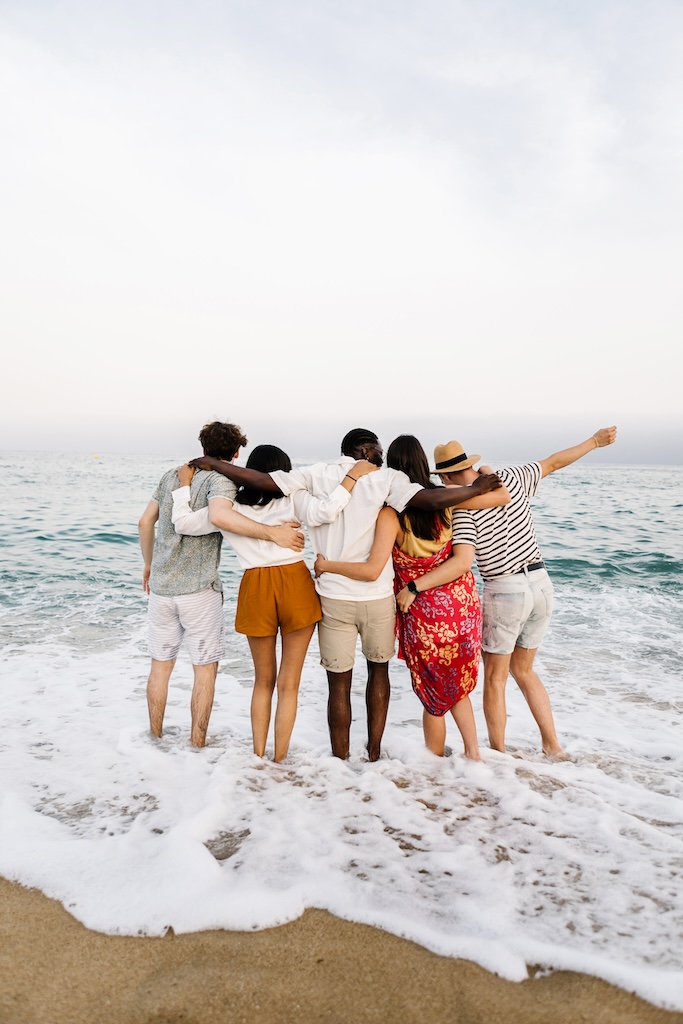 View from back of group of young people friends hugging each other and enjoying sunset at beach in California