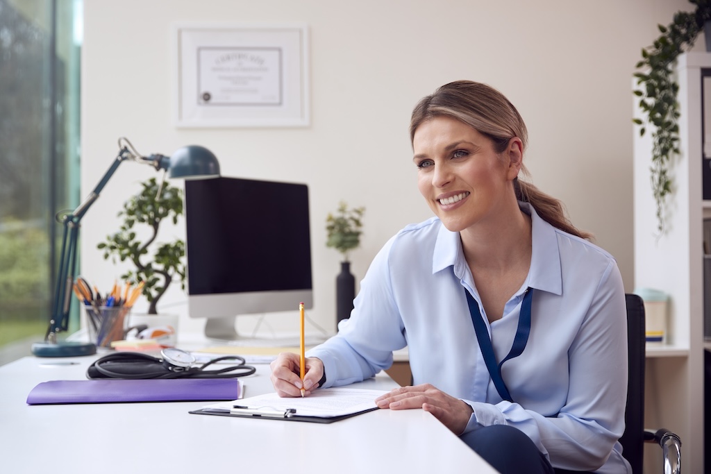 Smiling female clinician taking notes at her desk at trauma informed treatment center for mental health