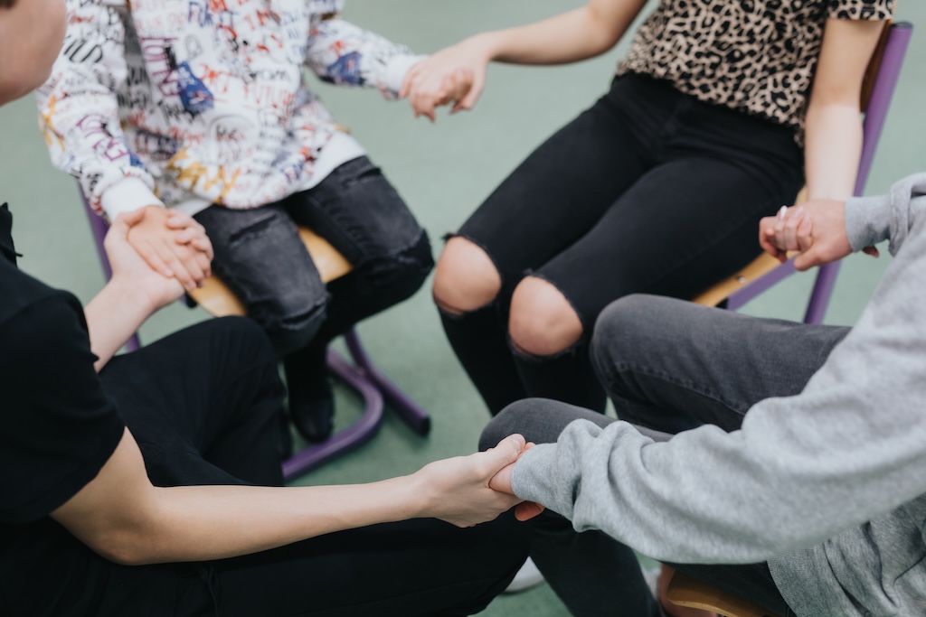 Closeup of four people in group therapy session, sitting together in a circle, holding hands