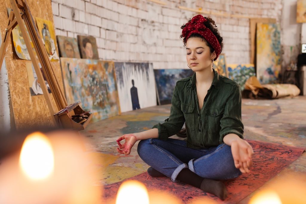 Young thoughtful woman with closing eyes sitting on yoga mat in lotus pose and meditating