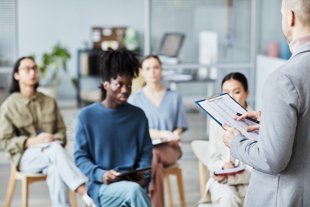 Back view of male clinician giving lecture to diverse group of people