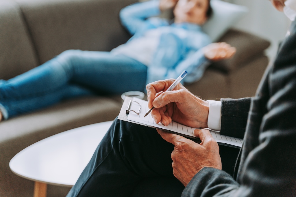 Woman sitting in psychiatrists office, close up view of psychiatrist writing on a clipboard during session