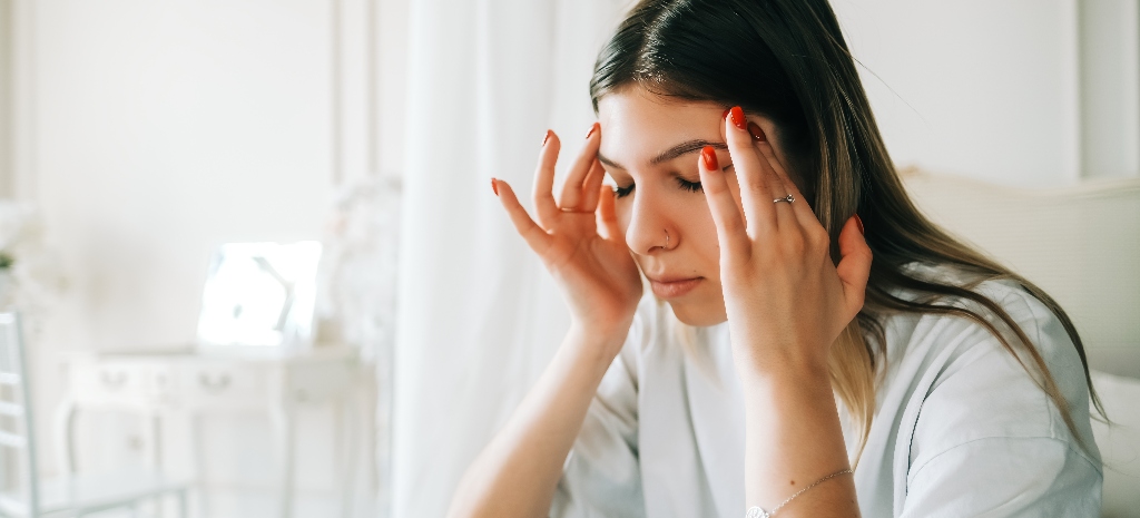 Young woman sitting with her head in her hands, rubbing her temples, experiencing agitation and restlessness