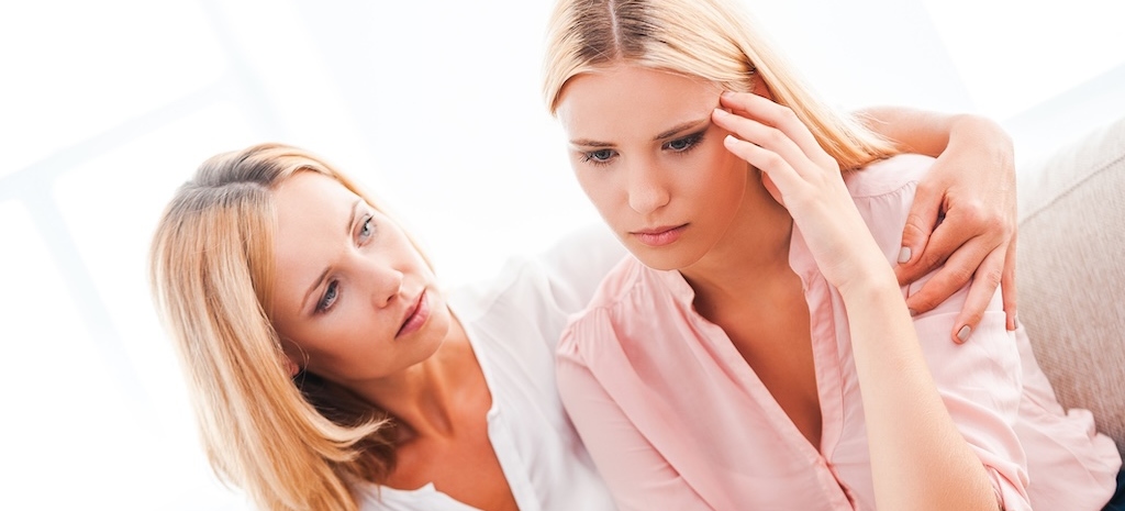 Beautiful mature woman consoling her depressed daughter while sitting on sofa