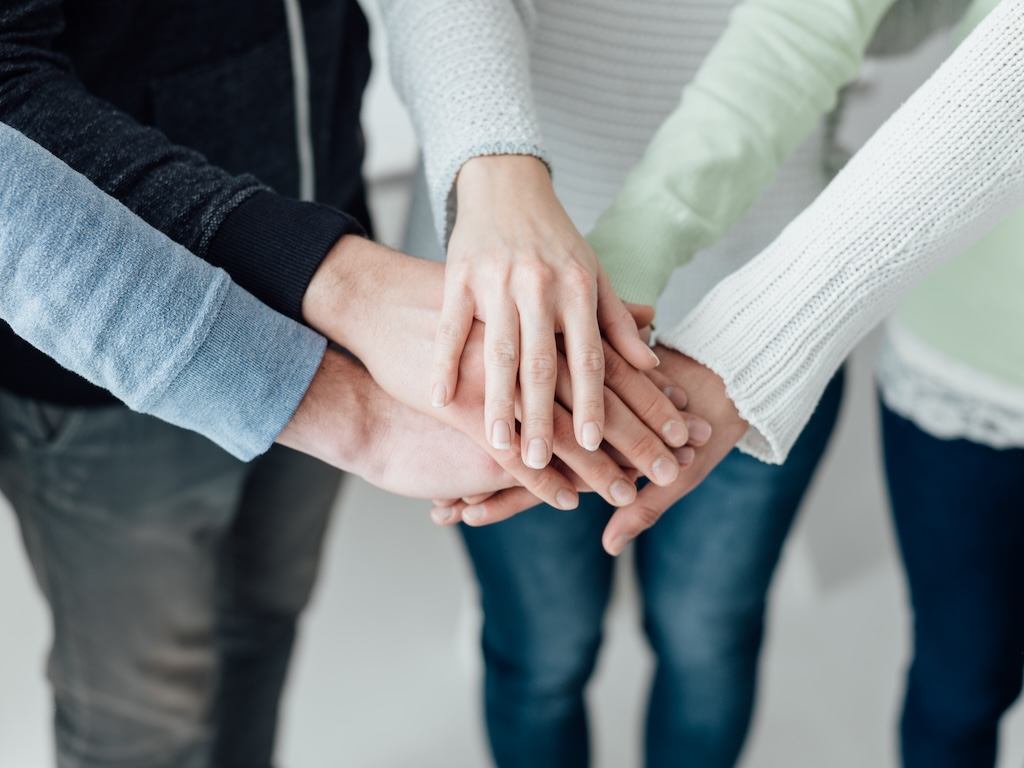 Young clients stacking hands together in show of support as they process trauma during group therapy session.