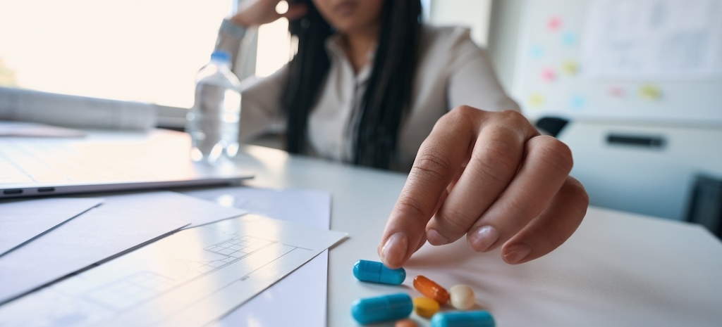 Defocused photo of employee seated at table reaching for prescription drug capsule 