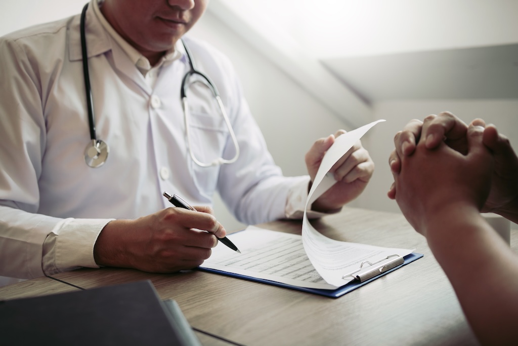 Doctor hand holding pen writing patient history list on note pad and talking to the patient about medication and treatment.