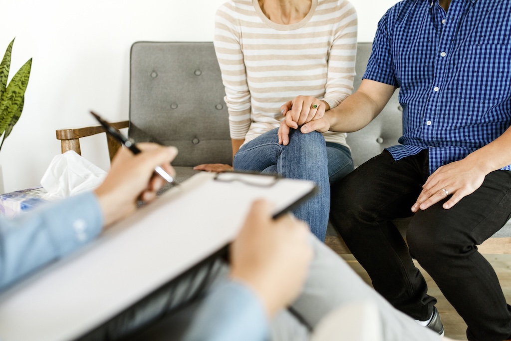 Couple holding hands sitting on a sofa during family therapy session.